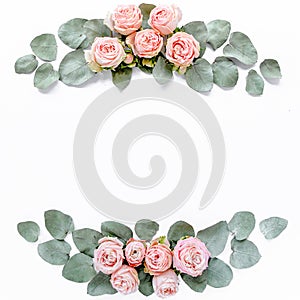 Frame made of pink roses, green leaves eucalyptus, branches, floral pattern on white background. Flat lay, top view