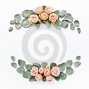 Frame made of pink roses, green leaves eucalyptus, branches, floral pattern on white background. Flat lay, top view