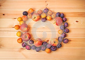 Frame made of ripe apples and fresh purple and yellow plums on wooden background