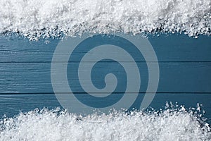 Frame made of snow on blue wooden background, top view. Christmas time