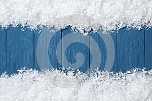 Frame made of snow on blue wooden background, top view with space for text. Christmas time