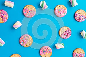 Frame made of tasty cookies with pink glaze and marshmallow on blue background. Flat lay. top view.