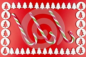 A frame made of white, wooden Christmas trees, three candy canes in the middle, isolated on a red background.