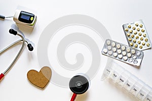 Frame of medical instruments, pills, stethoscope, pulse oximeter, wooden heart, pills blisters and container on white background