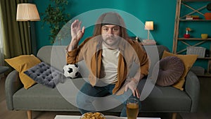 In the frame, a middle-aged man is sitting on a couch. He is watching a soccer match on television. Depicts excitement