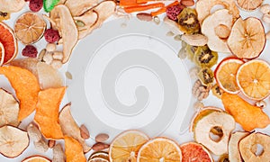 Frame of mixed dried fruit and vegetable chips, candied pumpkin slices, nuts and seeds on white marble background
