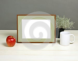 Frame mockup with plant pot, mug and apple on wooden shelf