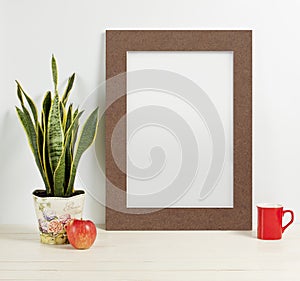 Frame mockup with plant pot, mug and apple on wooden shelf