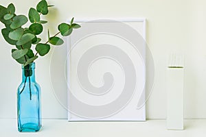 Frame mockup on white background, green eucalyptus branch in blue glass bottle, copyspace, blank tube