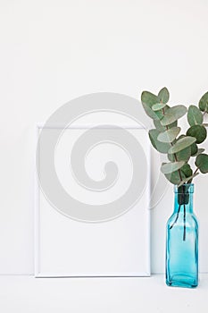 Frame mockup on white background, green eucalyptus branch in blue glass bottle, copyspace for text