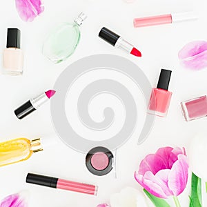 Frame of pink tulips flowers and cosmetics, lipstick with nail polish on white background. Top view. Flat lay feminine desk