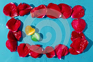 Frame of red rose petals on blue background. Two gem stone heart on rose petals in the middle. Abstract love and romance concept