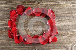 Frame of red rose petals on a wood background.