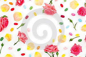 Frame of roses flowers and petals with bright sugar candy on white background. Flat lay, top view