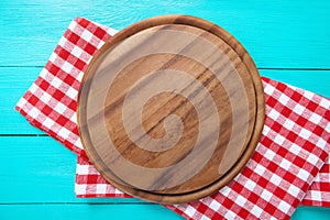 Frame of round cutting board and red plaid tablecloth. Blue wooden background in the cafe. Top view. Macro