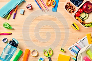 Frame of school supplies, backpack, kids lunch box on wooden table. Top view. Flat lay