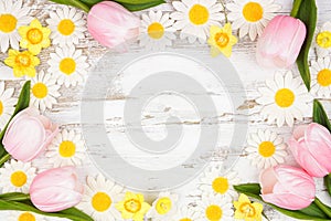 Frame of springtime flower decorations over a rustic white wood background