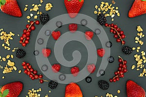 Frame of strawberries, blackberries, blueberries, raspberries, redcurrants and granola on a blackboard background, with space for