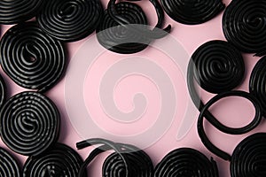 Frame of tasty black liquorice candies on pink background, flat lay. Space for text