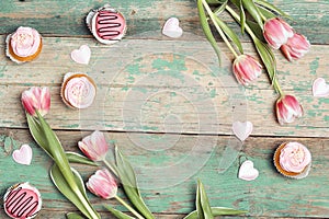 Frame of tasty cupcakes with tulips on vintage wooden table. Romantic love background. Copy space, overhead shot