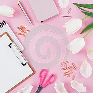 Frame with tulips flowers, mug of coffee, clipboard, clips and glasses on pink background. Blogger concept with copy space. Flat l