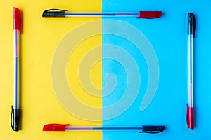 A frame of two-color ballpoint pens on a yellow and blue background. Flat lay, copy space, top view