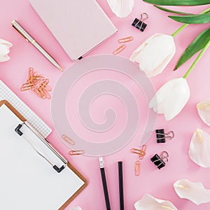 Frame with white flowers, clipboard, clips and pencil on pink background. Blogger concept with copy space. Flat lay, top view.