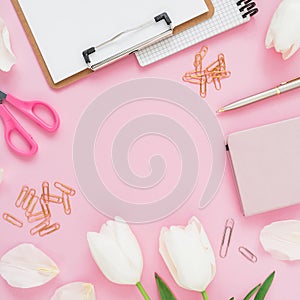 Frame with white flowers, mug of coffee, clipboard, clips and glasses on pink background. Flat lay, top view