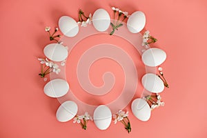 A frame of white flowers and white eggs on a pink background. Copy space, top view. Easter background.