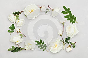 Frame of white rose flowers and leaves on light gray background from above, beautiful floral pattern, vintage color, flat lay