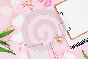 Frame of white tulips flowers, clipboard, clips and scissors on pink background. Blogger concept. Flat lay, top view.