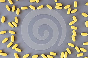 Frame from yellow vitamins or pills on gray background, close-up, copy space. Nutritional supplements concept, health, vitamins,