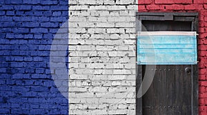 France flag painted on brick wall and closed door with medical mask protected