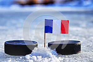 Vlajka Francúzska na špáradlo medzi dvoma hokejovými pukmi. Francúzsko bude hrať na Svetovom pohári v skupine A. Majstrovstvá sveta 2019 IIHF