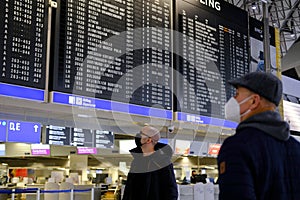 Frankfurt, Germany - January 2022: two men in medical mask looks at schedule of aircraft flights on an electronic scoreboard,