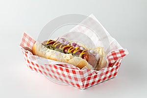 A frankfurter in a disposable checkered tray isolated against a white background.