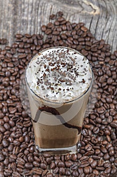 Frappuccino with ice in take away cup, with straws and grains of coffee on a wooden table, copy space