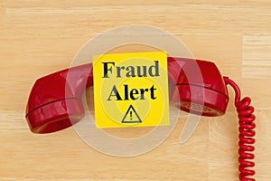 Fraud alert on sticky note with a retro red phone on textured wood desk photo