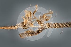 Frayed rope near to break on gray background