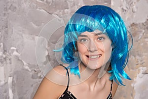 Freak concept. Lady on smiling face posing in blue wig, concrete wall background. Woman with blue hair looks unordinary photo