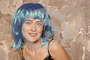 Freak concept. Lady on smiling face posing in blue wig, concrete wall background. Woman with blue hair looks unordinary photo