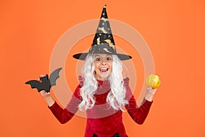 Freakishly wicked Halloween. Little wicked witch child hold bat and pumpkin. Happy girl wear wicked witch costume. Small