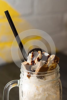 Freakshake in jar with cocktail straw, chunks of chocolate and cookies, on dark wooden table. Vertical