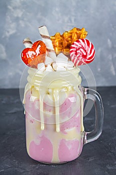 Freakshake from pink smoothie, cream. Monstershake with lollipops, waffles and marshmallow. Extreme milkshake in a Mason jar. Gray