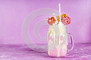 Freakshake from pink smoothie, cream. Monstershake with lollipops, waffles and marshmallow. Extreme milkshake in a Mason jar. Pink