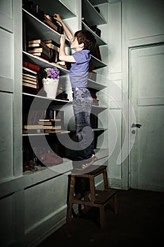 Freckled red-haired little boy searching book on bookcase