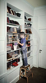 Freckled red-haired little boy searching book on bookcase