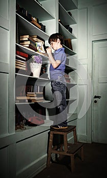 Freckled red-haired little boy searching book on bookcase