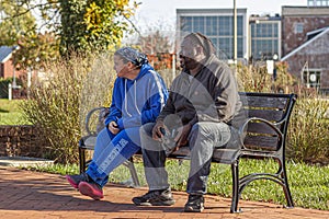 An interracial couple caucasian woman and African American man are sitting together on a park bench.