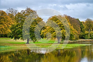 Frederiksborg Castle Park with mighty deciduous trees, reflected in the created lake